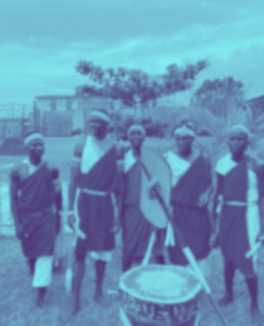 A blurred image of a group of men in traditional Burundian attire, including headbands and wraps, standing together with a drum in the foreground
