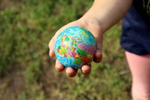 A child's hand holding a small colorful globe in a natural outdoor setting