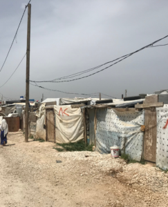 Makeshift shelters in a Syrian refugee camp in Lebanon, with a person walking in the background