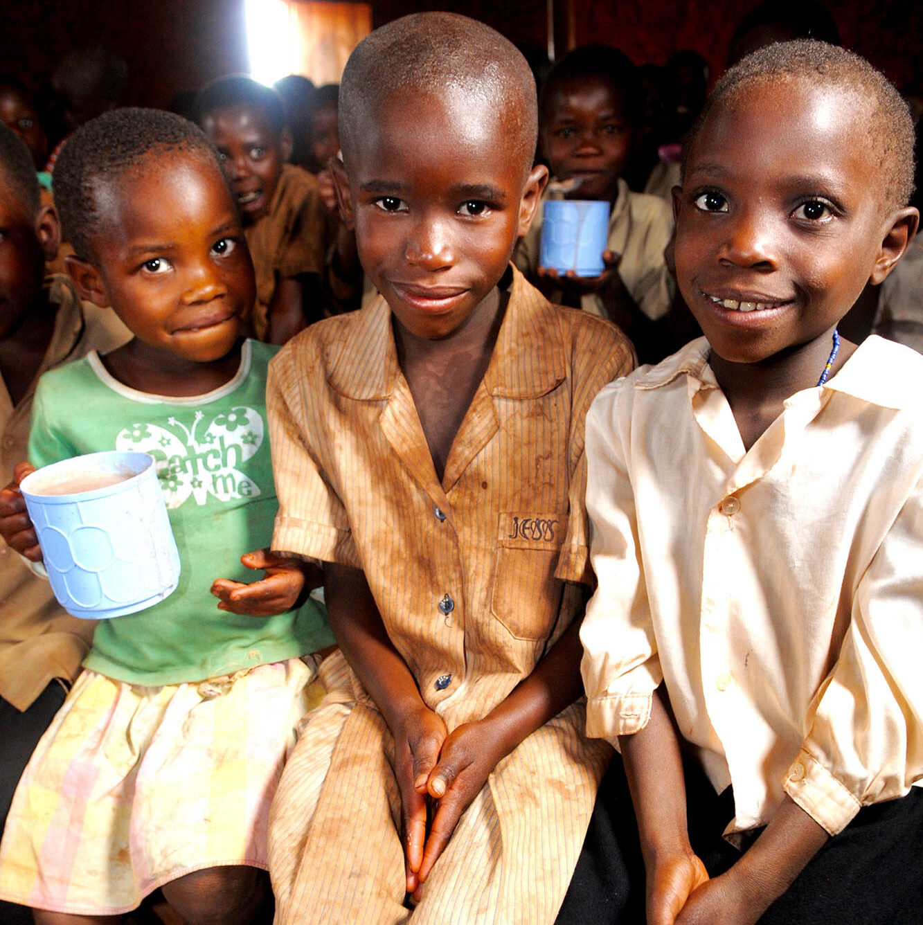hree young children smiling for the camera in a community setting in Burundi