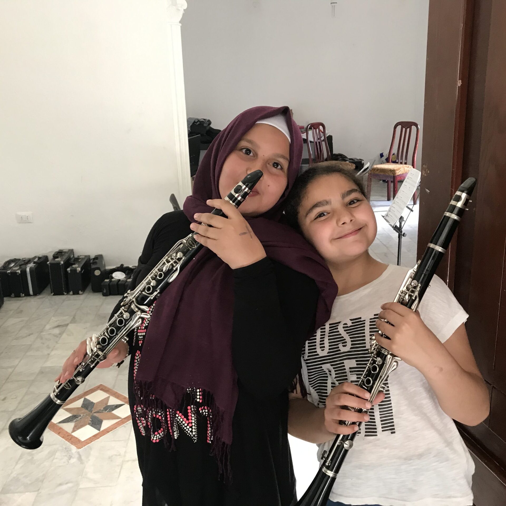 Two young Syrian refugee girls in Lebanon holding clarinets, smiling at the camera