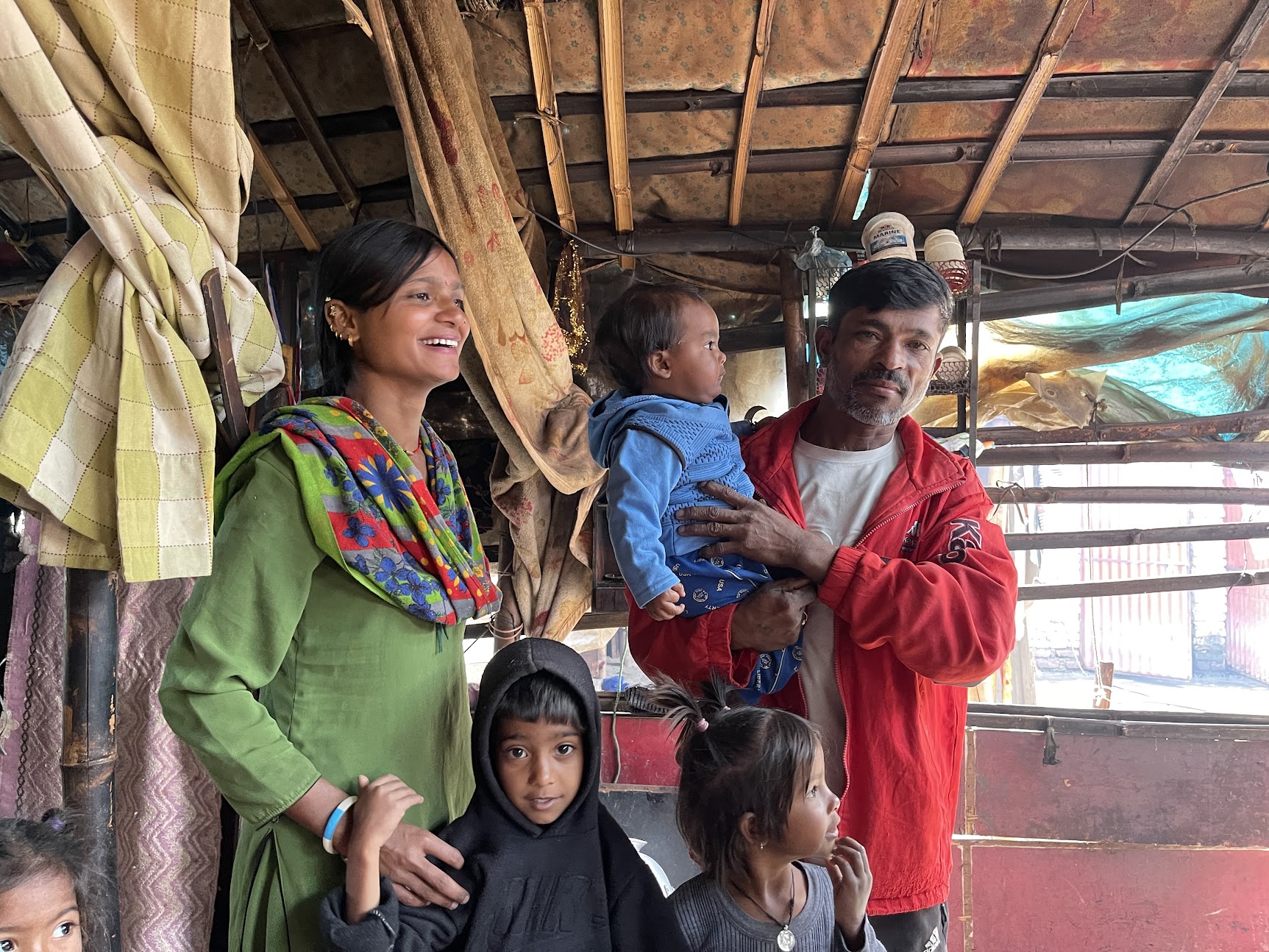 A family in Nepal with two adults and three children posing for a photo inside a room with a rustic interior.